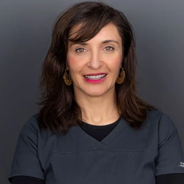 Retrato de una profesional de la clínica con uniforme oscuro sonriendo sobre fondo gris